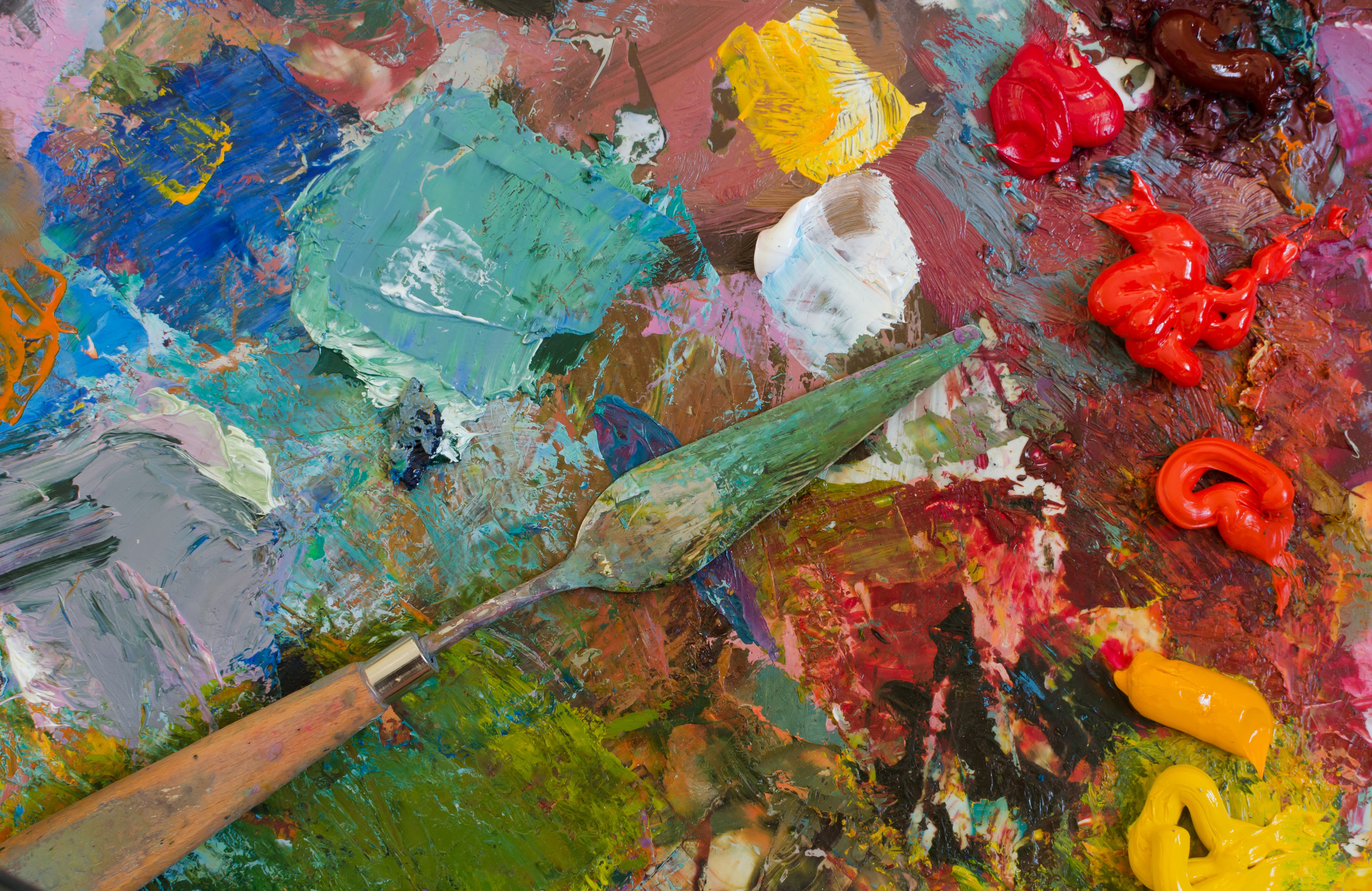 Artist's touch shown by his tools of a palette knife and a large array of paint colors spread on a messy art surface